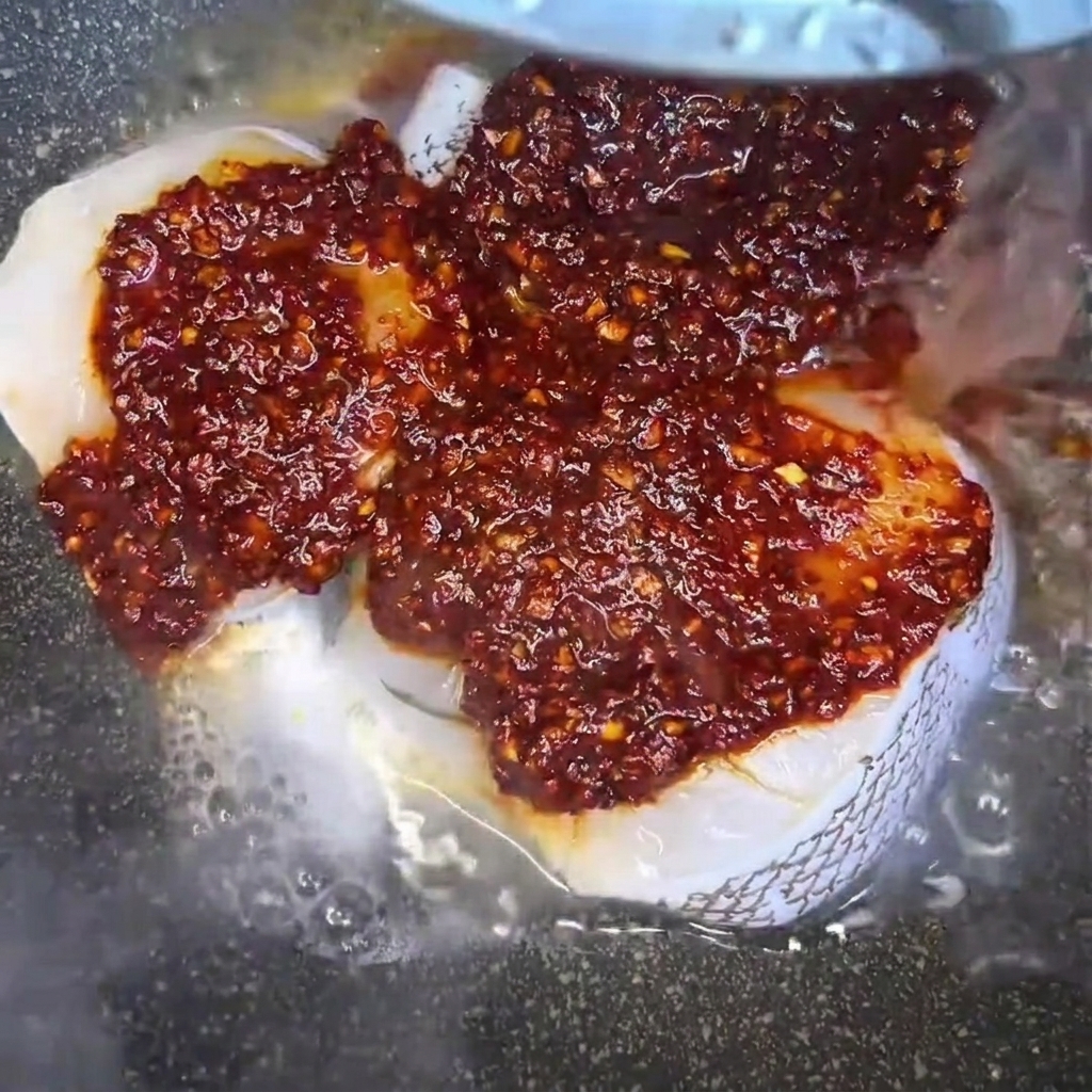 Water being poured into a pan containing seasoned raw cod fillets, creating a savory braising liquid.