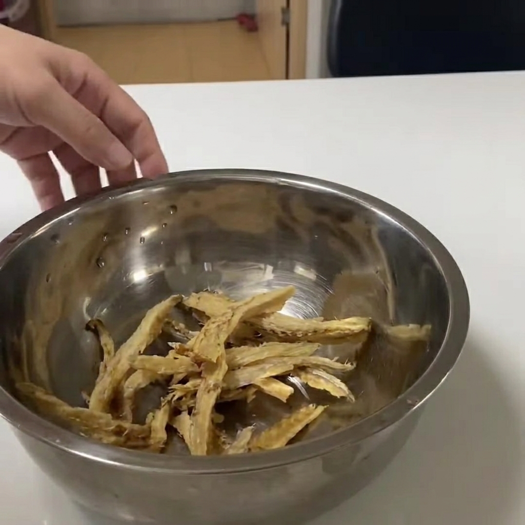 Dried pollack strips submerged in clear water within a metal mixing bowl.