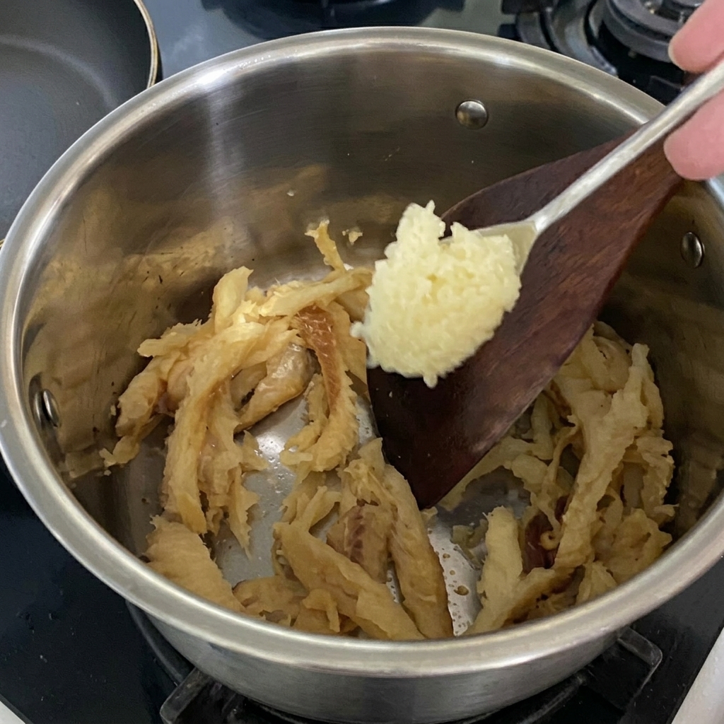 A spoonful of minced garlic being added to the stir-frying yellow pollack in the pot.