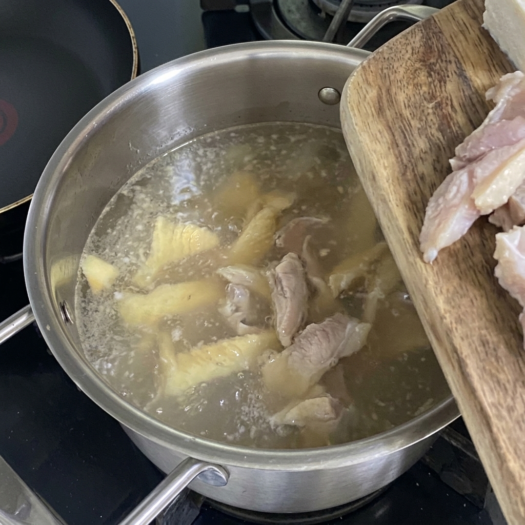 Fresh tofu cubes being dropped into the simmering, light-colored pollack broth.