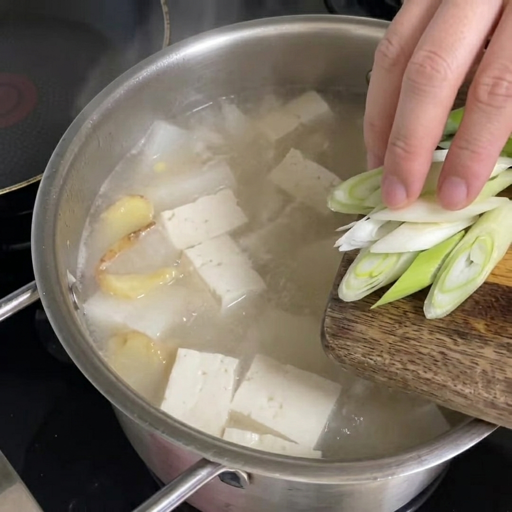 Freshly chopped green onions being scattered over the boiling pollack soup.