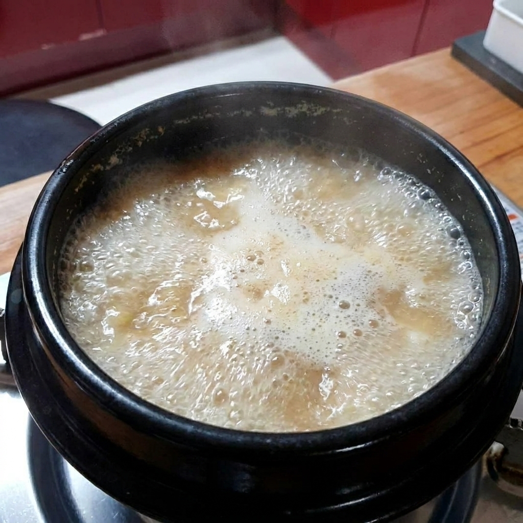 Minced garlic being added to the boiling soybean paste stew.