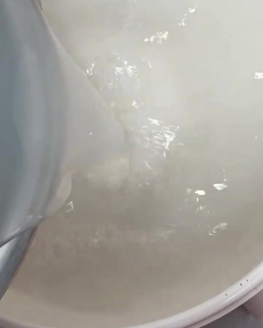 Clear white rice water being poured into a large cooking pot.