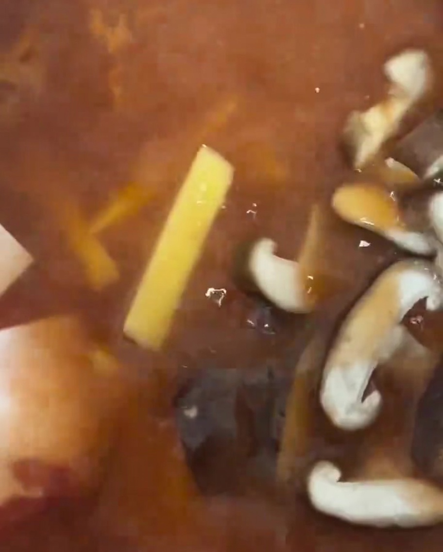 Slices of fresh shiitake mushrooms being placed into the stew.