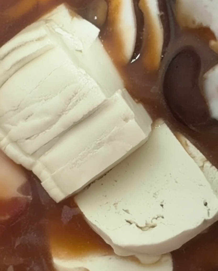 Fresh, soft white tofu slices being layered into the bubbling stew.