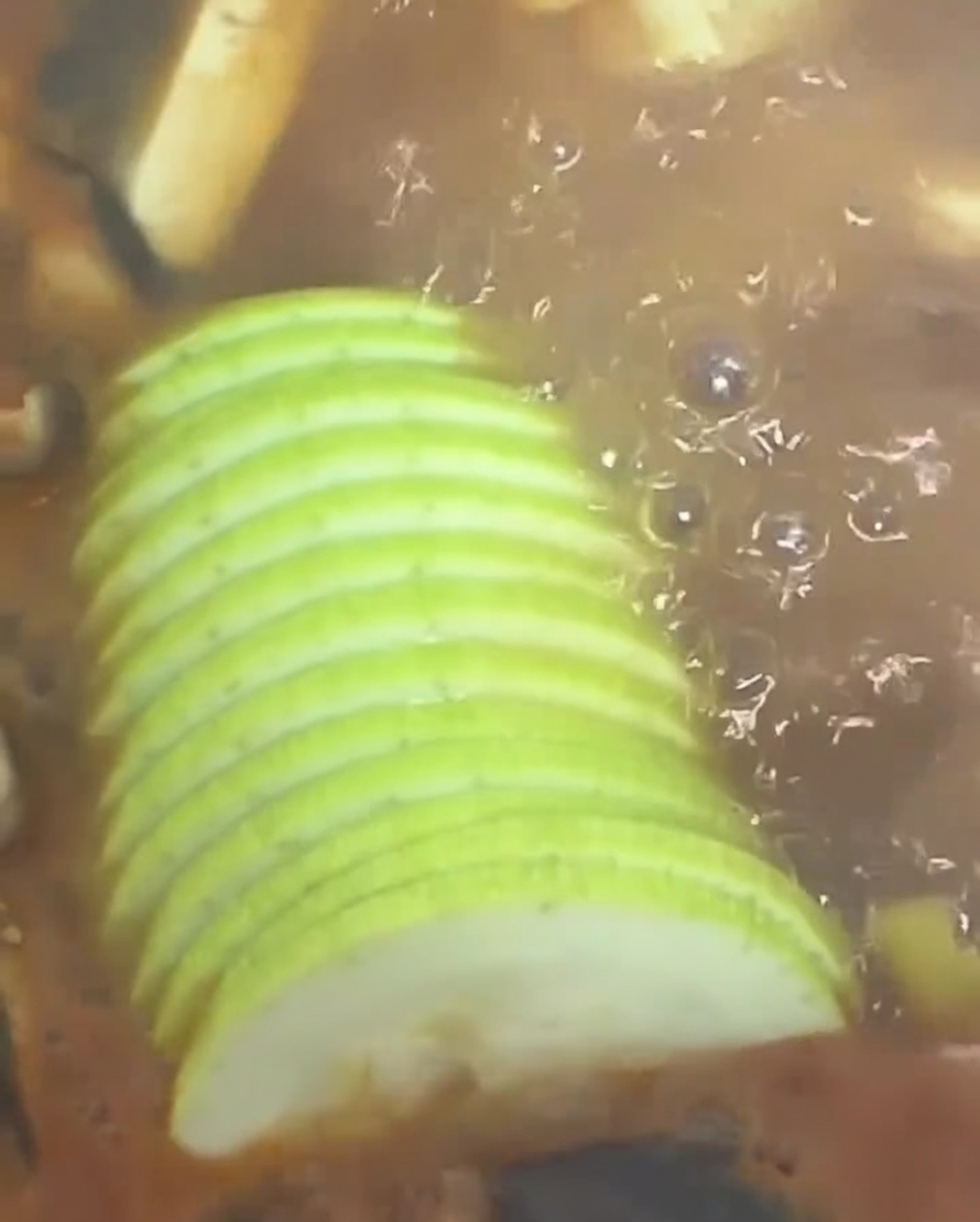 Slices of fresh green squash being added to the bubbling Korean stew.