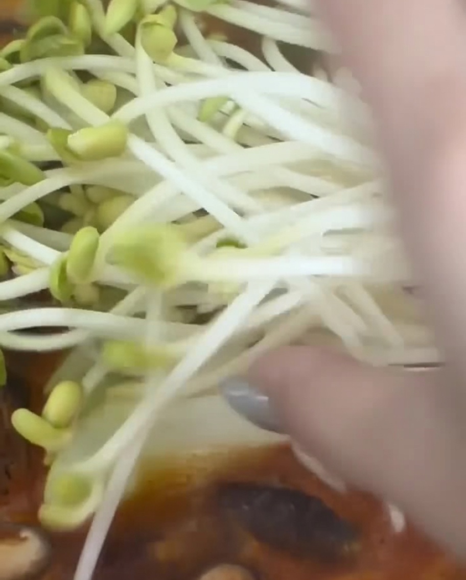 A handful of fresh soybean sprouts being added to a pot of simmering Korean stew.