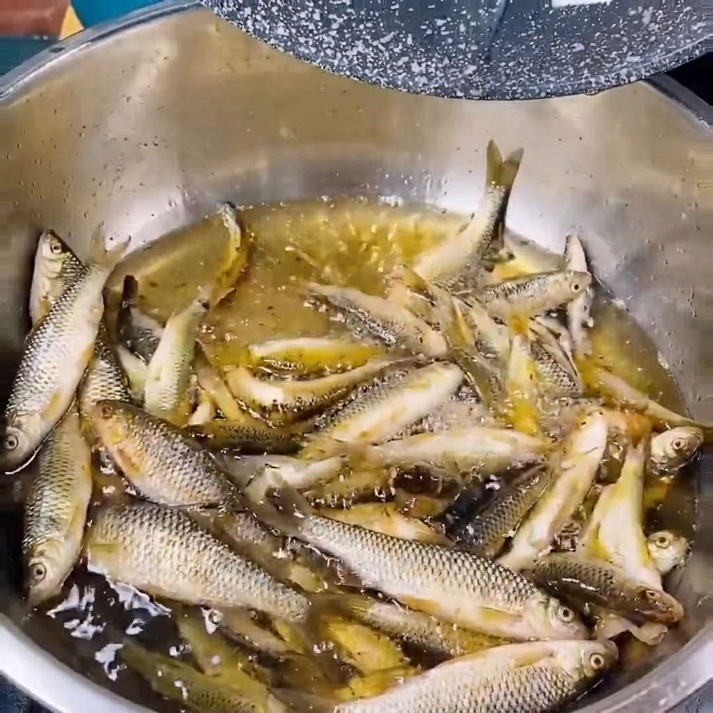 Small fresh river fish being rinsed in a metal bowl filled with clear water.