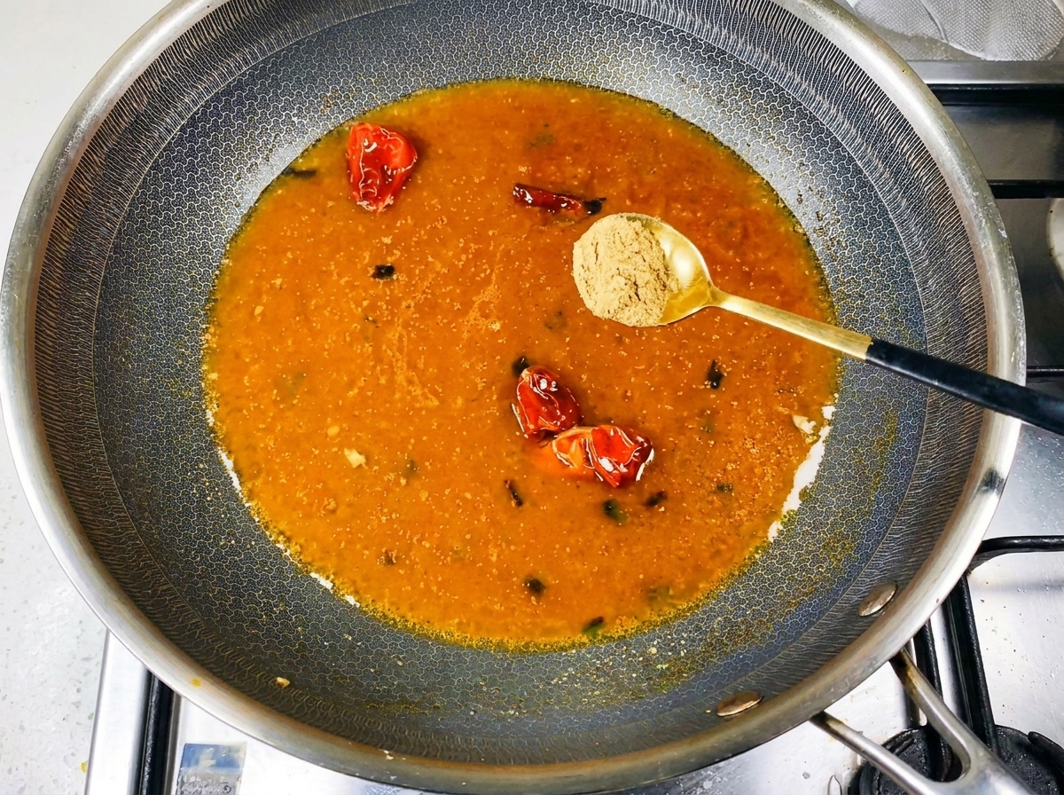 Spice powder being sprinkled into a simmering orange-colored broth in the wok.