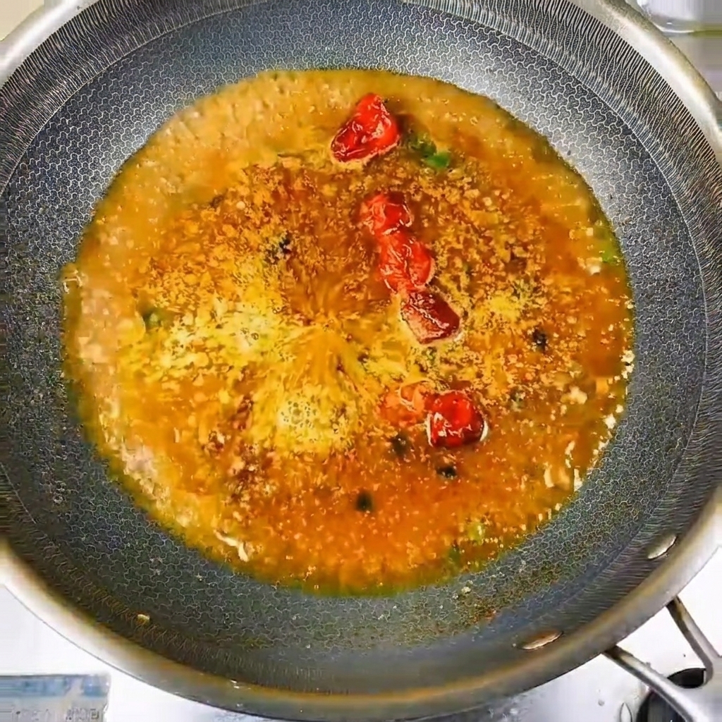 Small, fresh river fish meticulously arranged in a circular formation inside the seasoned, bubbling cooking liquid.