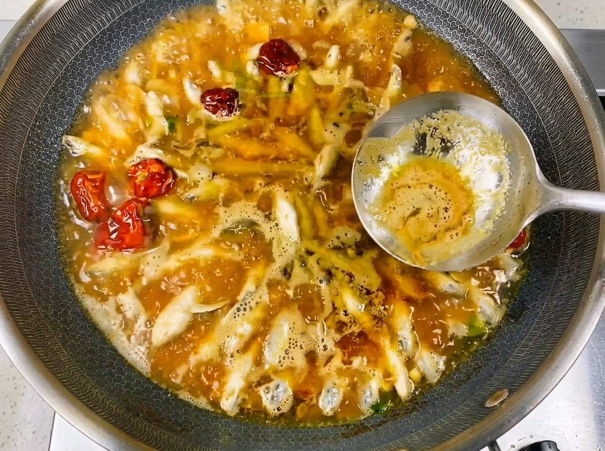 A close-up of the small river fish boiling in a rich, savory broth with visible bubbles.