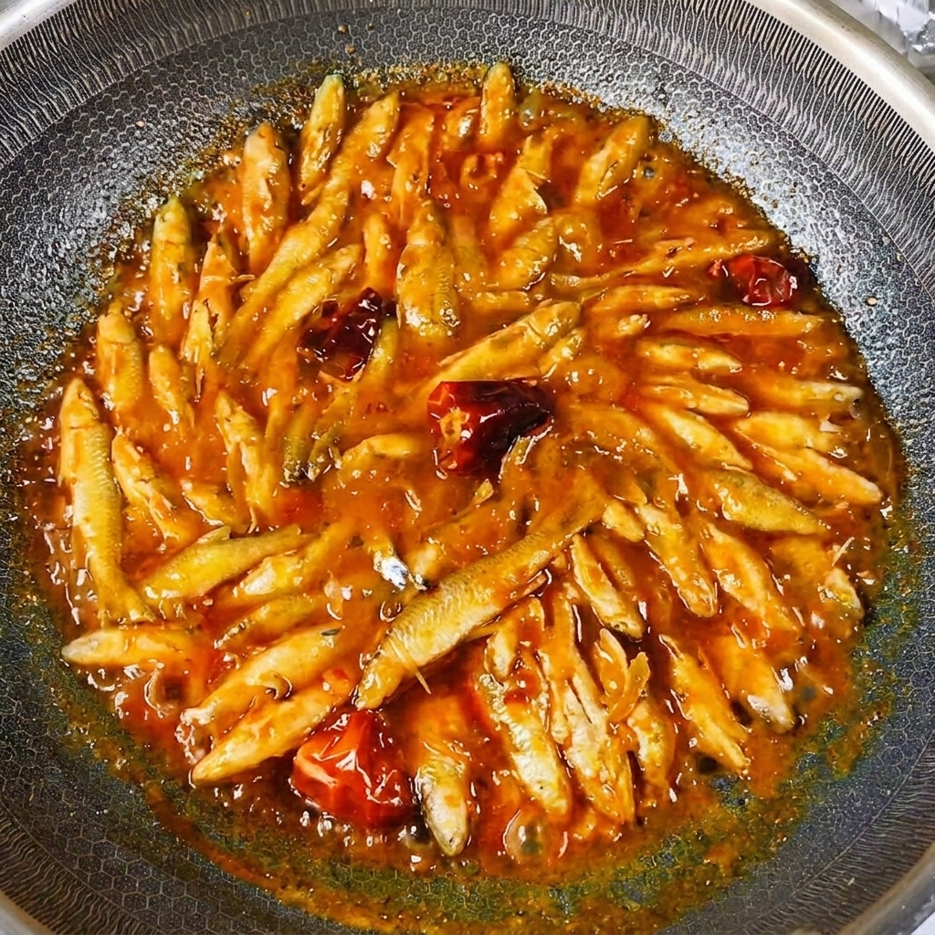 The cooked small river fish glistening with a thick, reduced savory sauce in the wok.