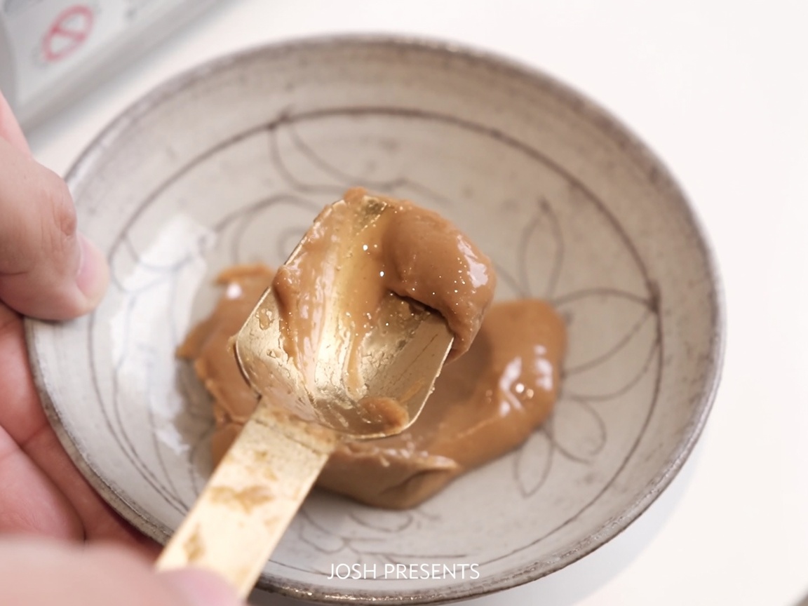 Miso paste being stirred in a small bowl with hot water using a gold spoon.
