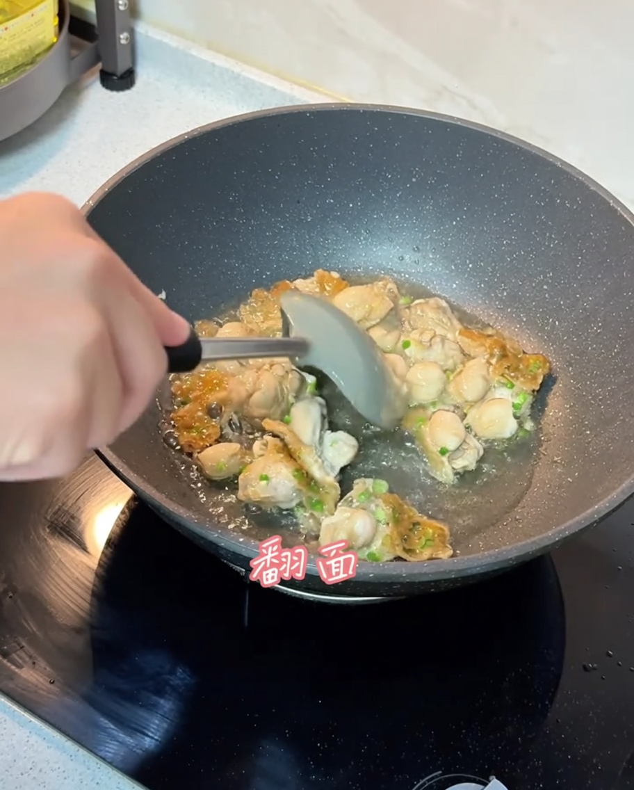 The oyster mixture being flipped in the pan with a spatula, showing a golden-brown cooked surface.