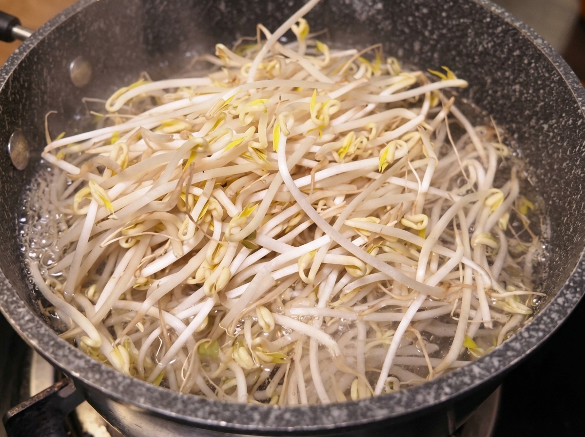 Fresh mung bean sprouts boiling rapidly in a dark cooking pot.