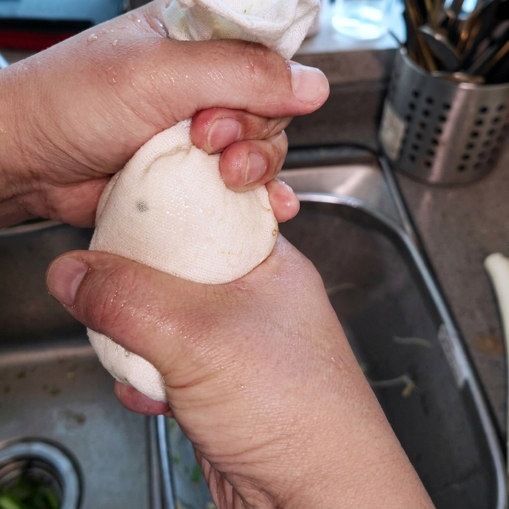 A block of tofu being squeezed inside a piece of white fabric over a kitchen sink.