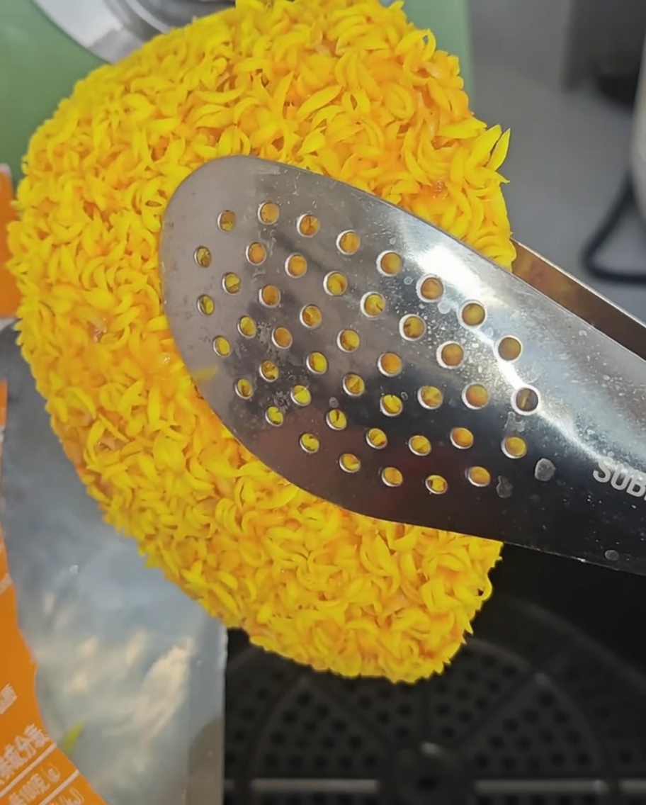 Frozen chicken fillets being arranged inside the air fryer basket using metal tongs.