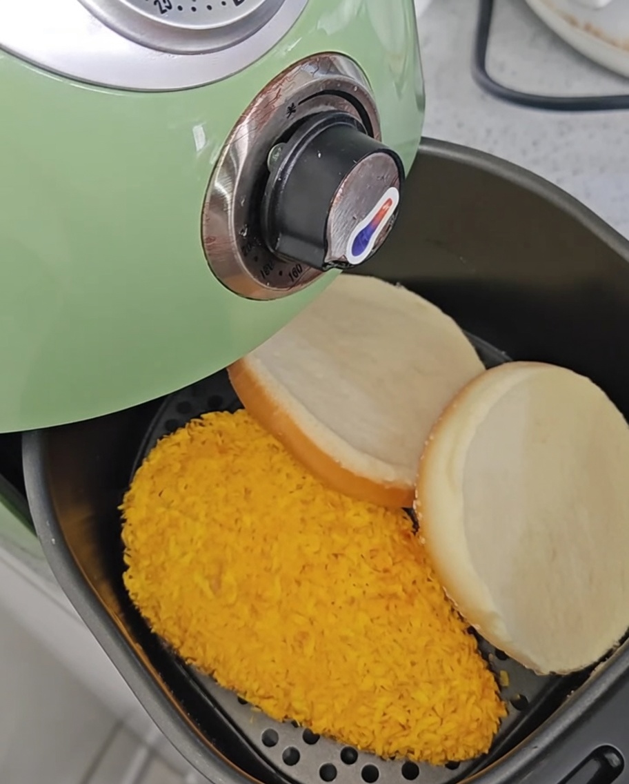 Chicken fillets inside the air fryer after being flipped, with two burger buns placed beside them.