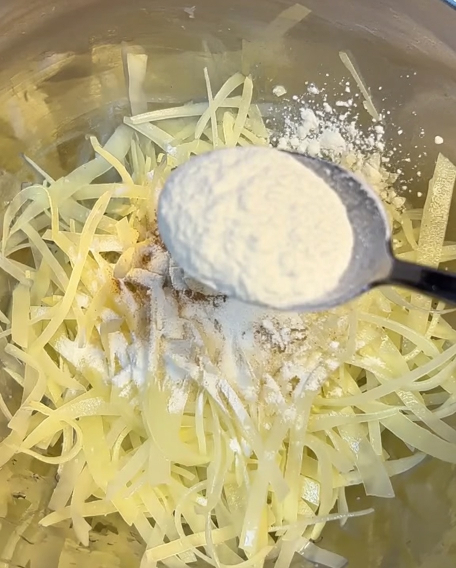 Bowl of shredded potatoes being coated with a mixture of flour and cornstarch.