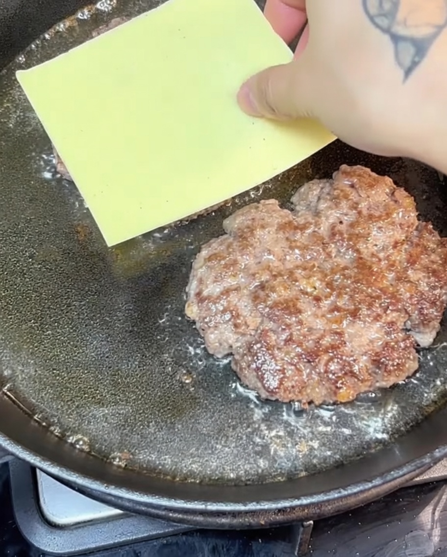 Cheesy beef patties sizzling in a hot cast iron skillet.