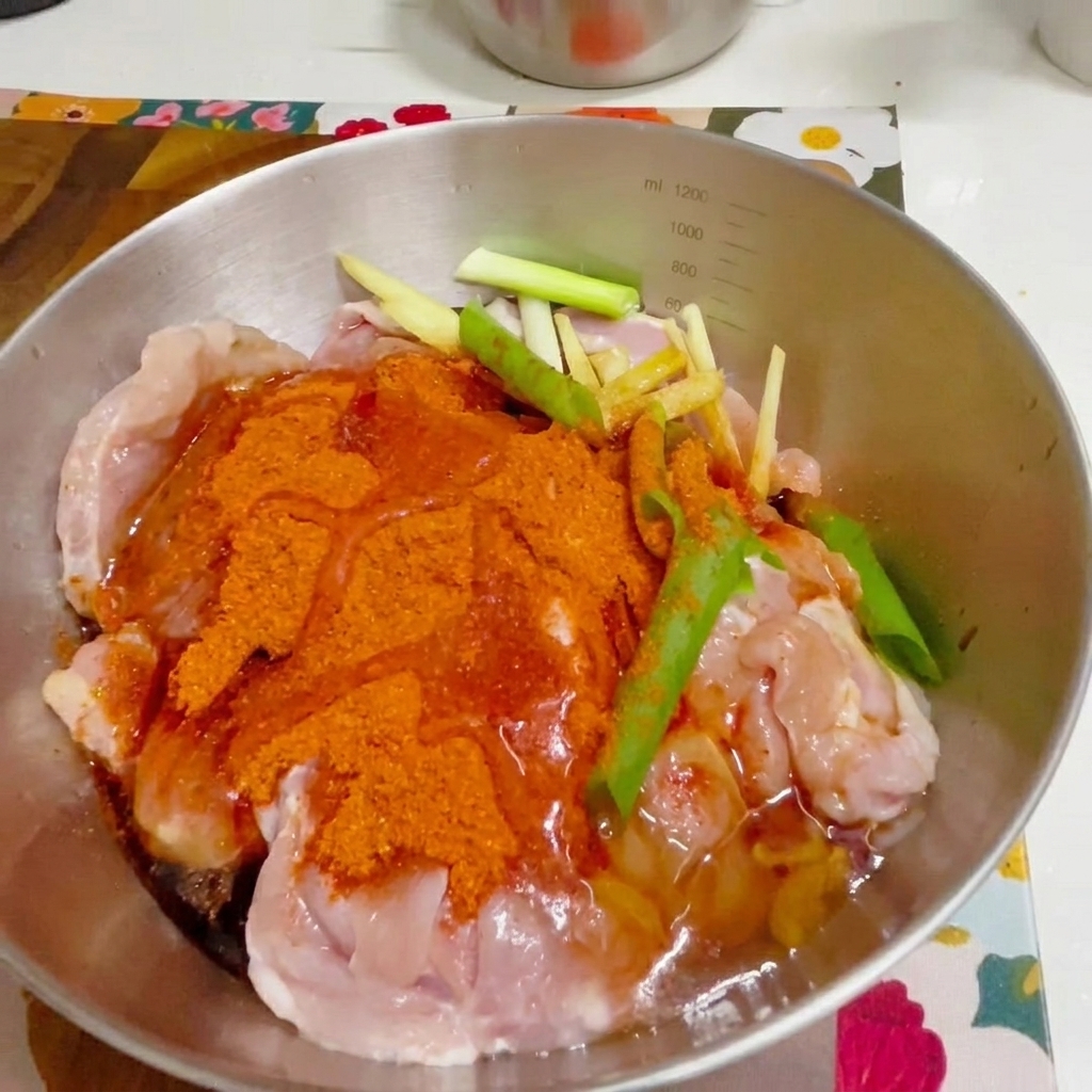 A gloved hand mixing seasoned chicken in a metal bowl.