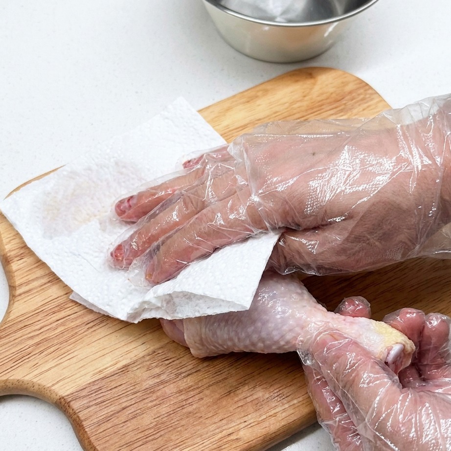 Raw chicken leg being prepared on a wooden cutting board with paper towels.