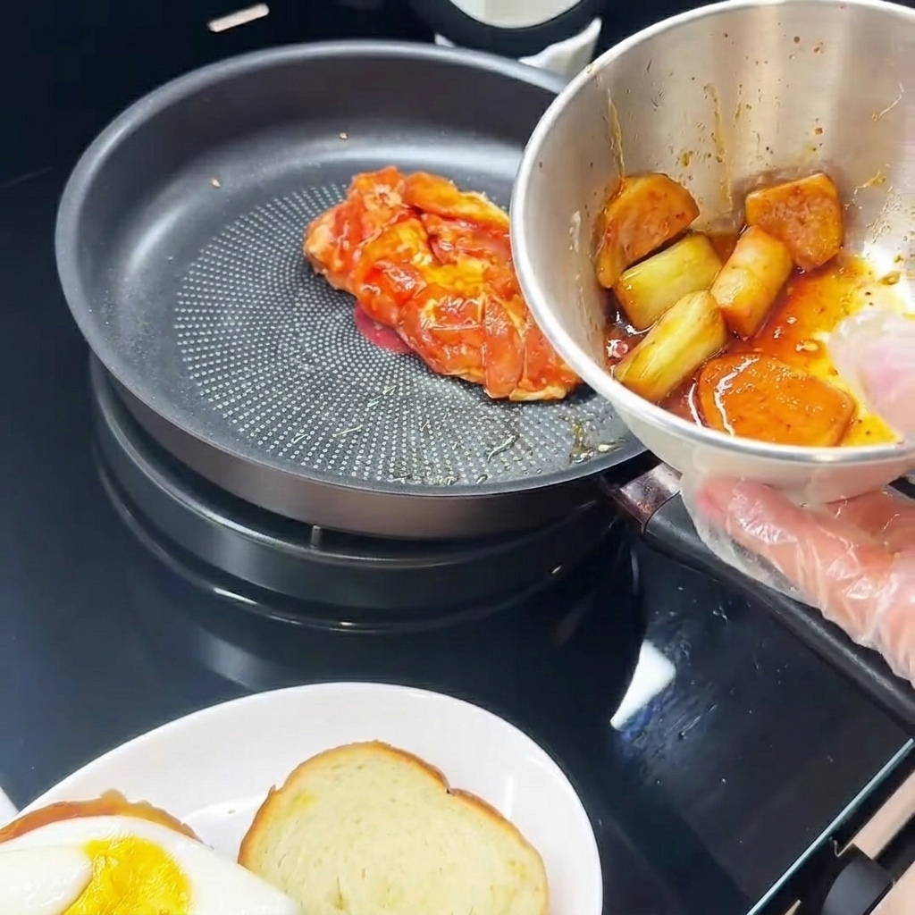 Marinated chicken thigh cooking in a pan, skin-side down, next to a plate with a fried egg.
