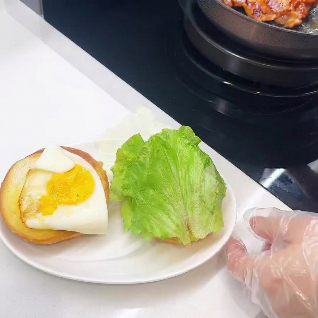 A close-up view of the burger assembly, showing the chicken, cheese, egg, and lettuce being stacked on the bun.