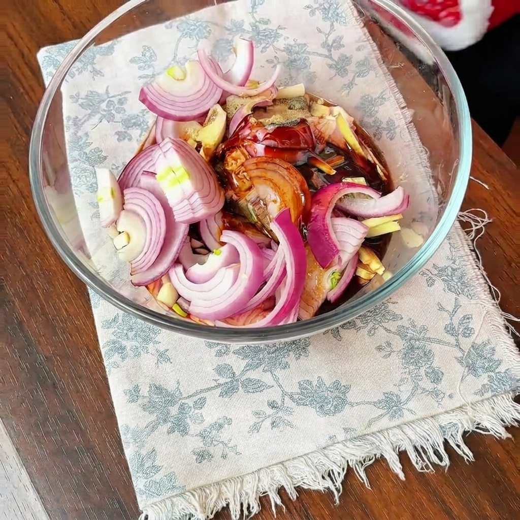 Chicken thighs, sliced onions, and dark marinade seasonings mixed together in a large glass bowl.