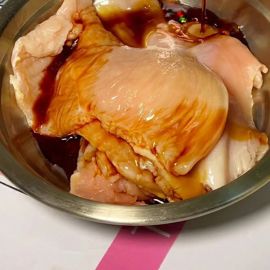 Raw chicken slices in a mixing bowl being coated with a dark, savory marinade.