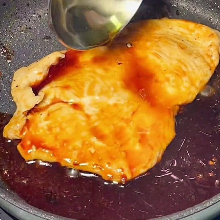 Rich, glossy teriyaki sauce being poured over golden-brown chicken in a skillet.