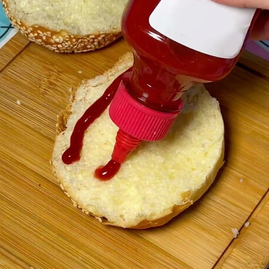 A swirl of red ketchup being applied to the center of a toasted sesame seed bun.