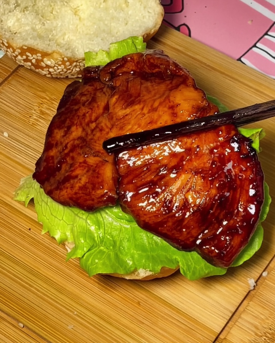 Teriyaki chicken, tomato, and cheese being layered onto the burger bun.