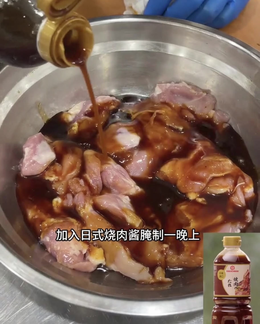 Boneless chicken thighs soaking in a pool of dark Japanese teriyaki sauce within a stainless steel mixing bowl.
