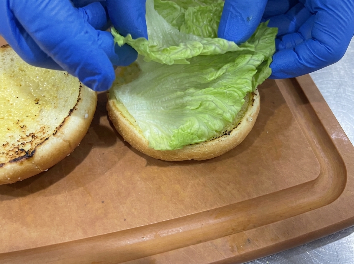 Crisp green lettuce leaves being arranged onto the toasted bottom half of a burger bun.