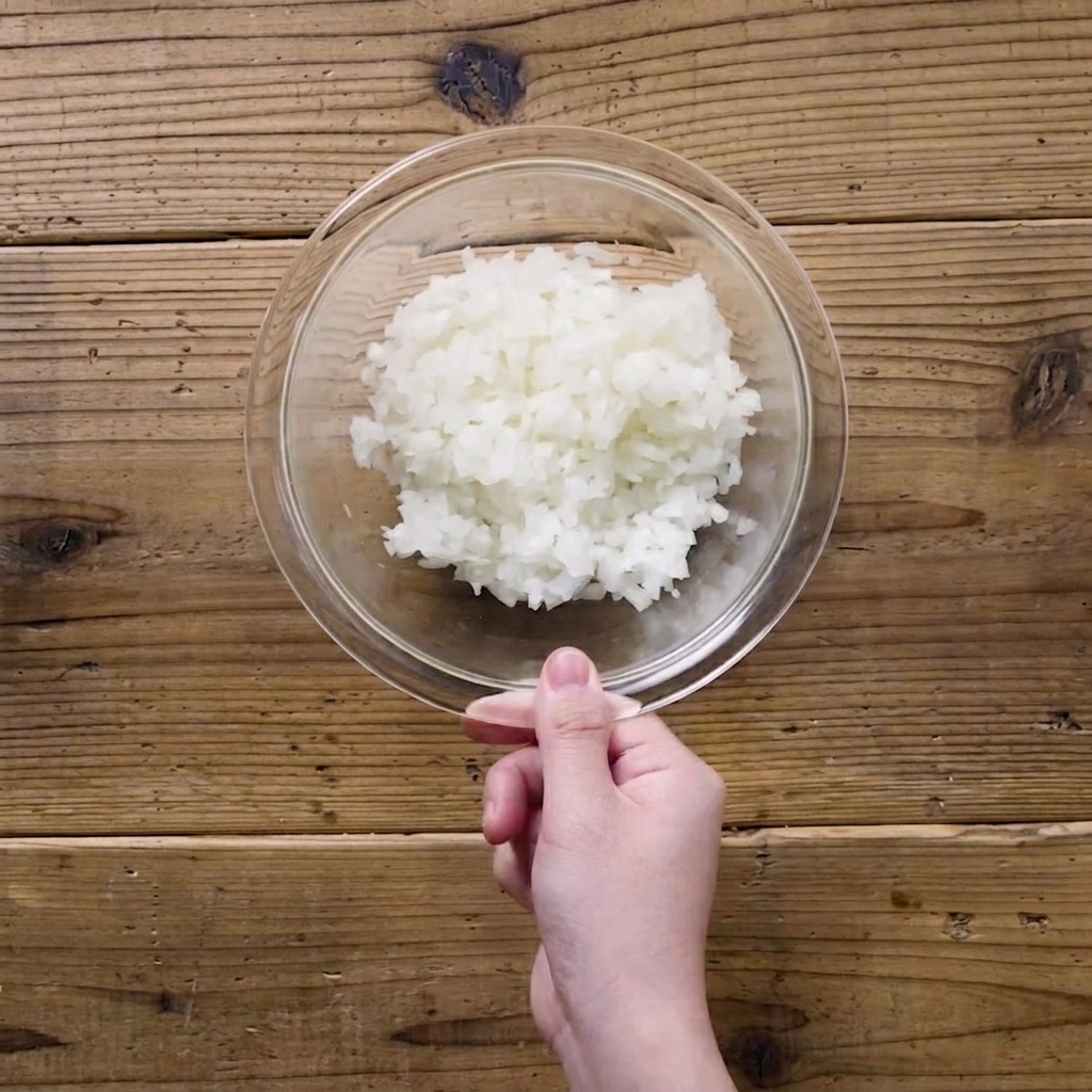 Finely chopped onions in a clear glass bowl covered with plastic wrap.