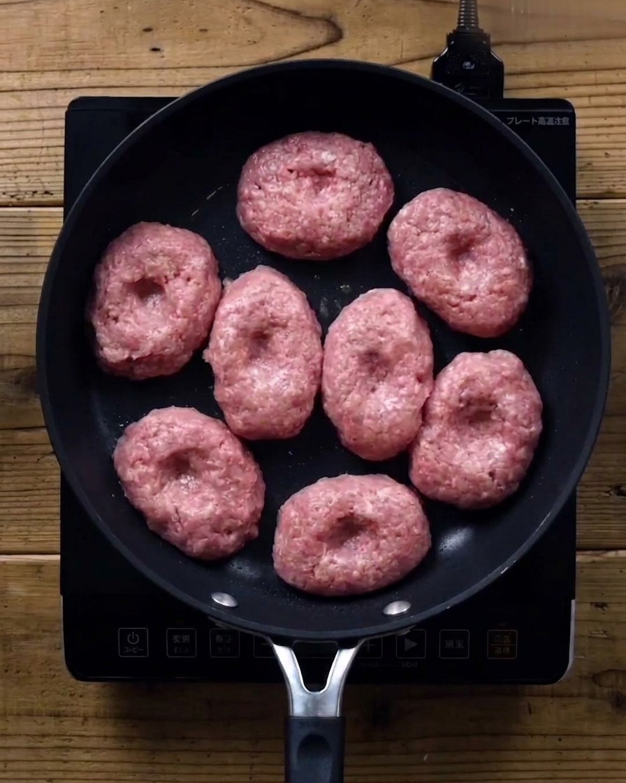 Patties in a frying pan covered with a glass lid.