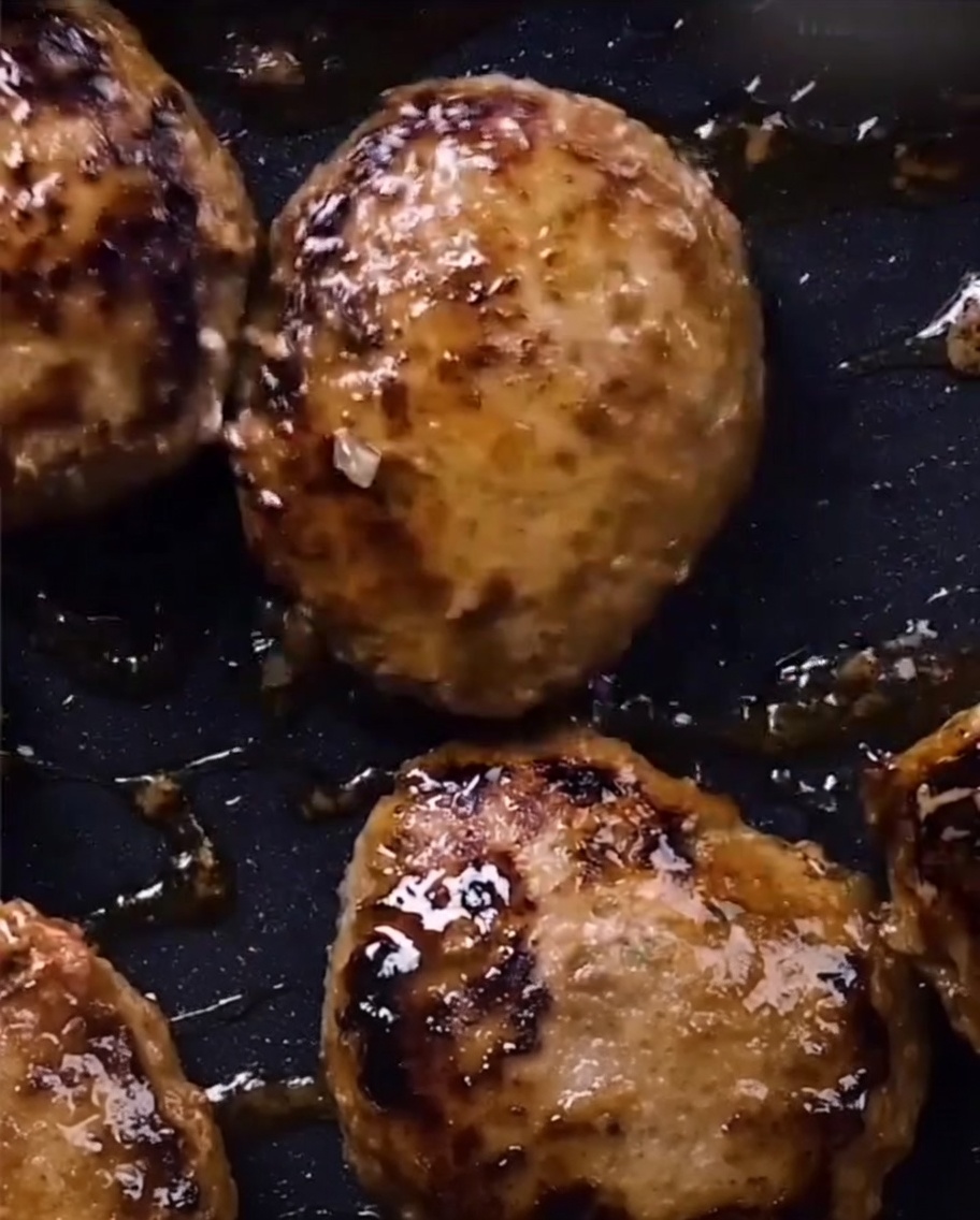 Hamburger steaks glistening with a dark, thick teriyaki glaze in a frying pan.
