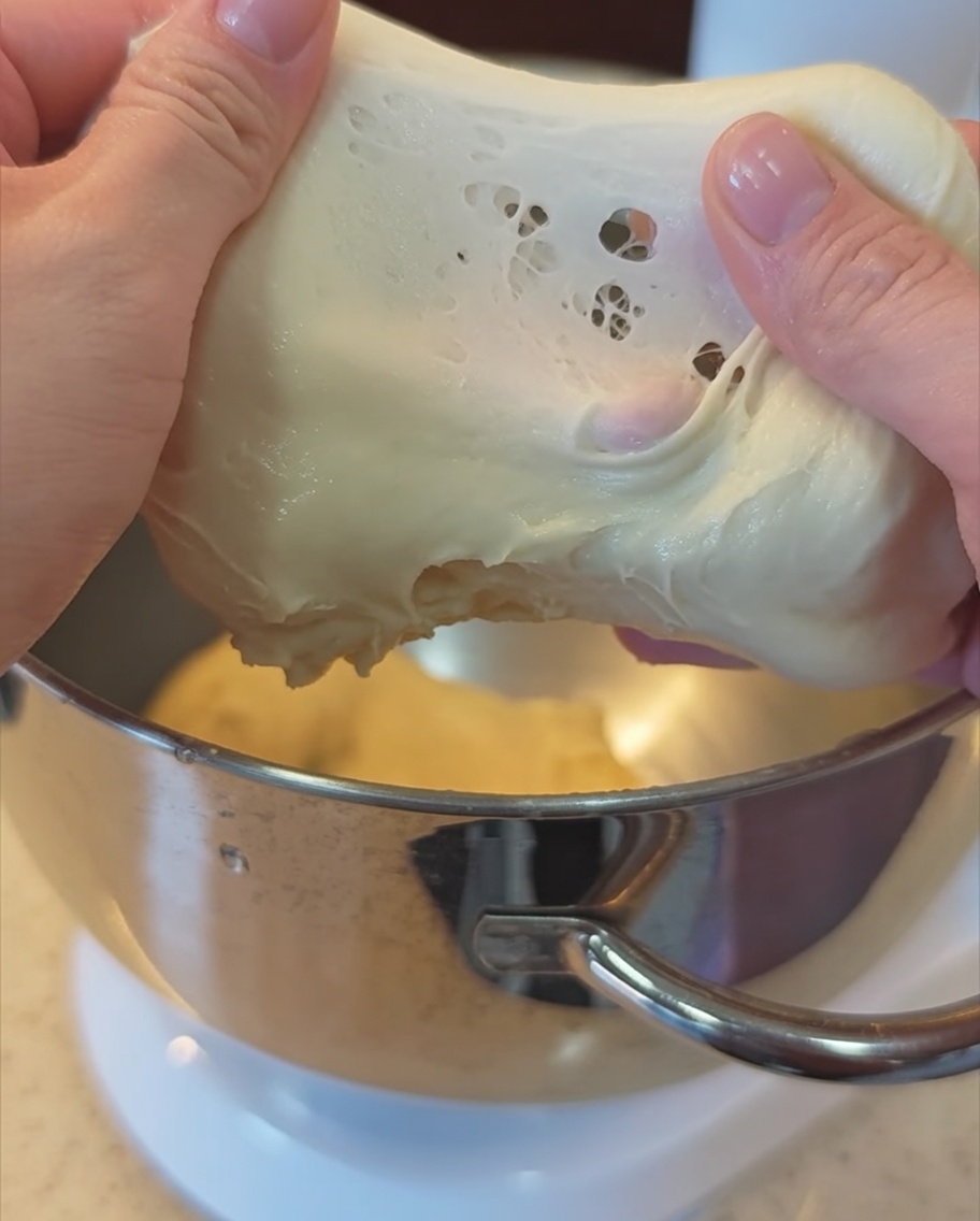 A pair of hands stretching a piece of smooth, elastic dough to check for the windowpane stage.