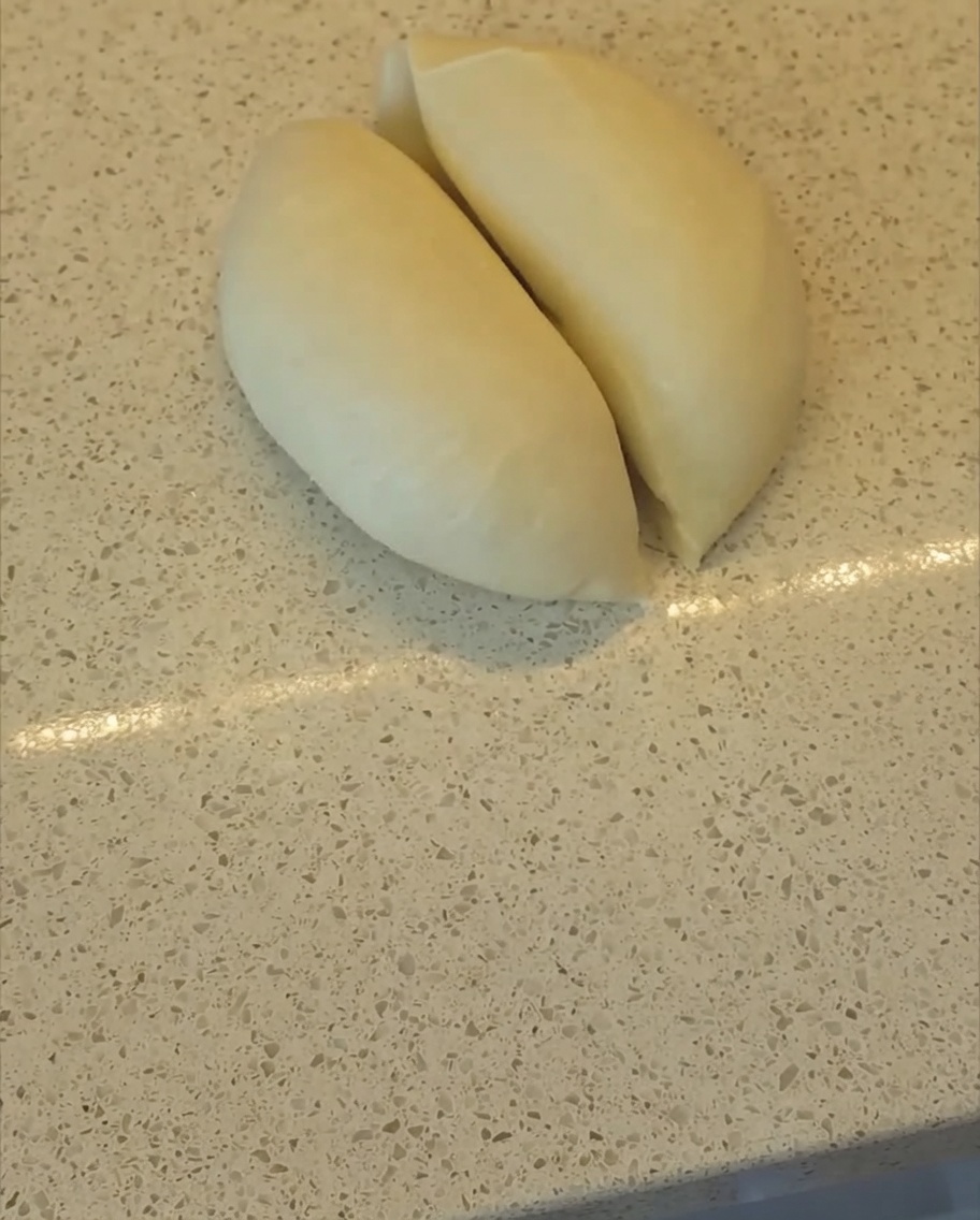 A bench scraper cutting a smooth mass of dough into two equal halves on a clean kitchen counter.