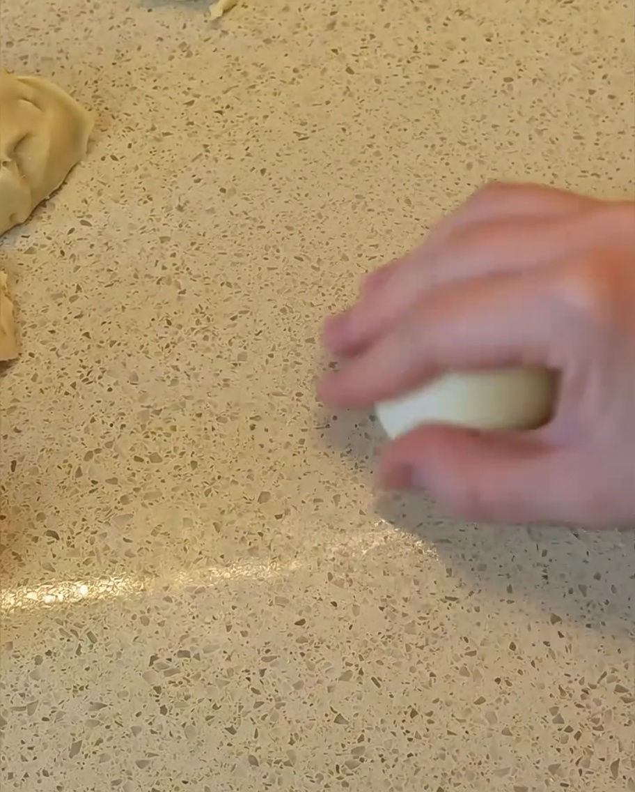 A hand rolling a piece of dough on the countertop to shape it into a smooth, round ball.