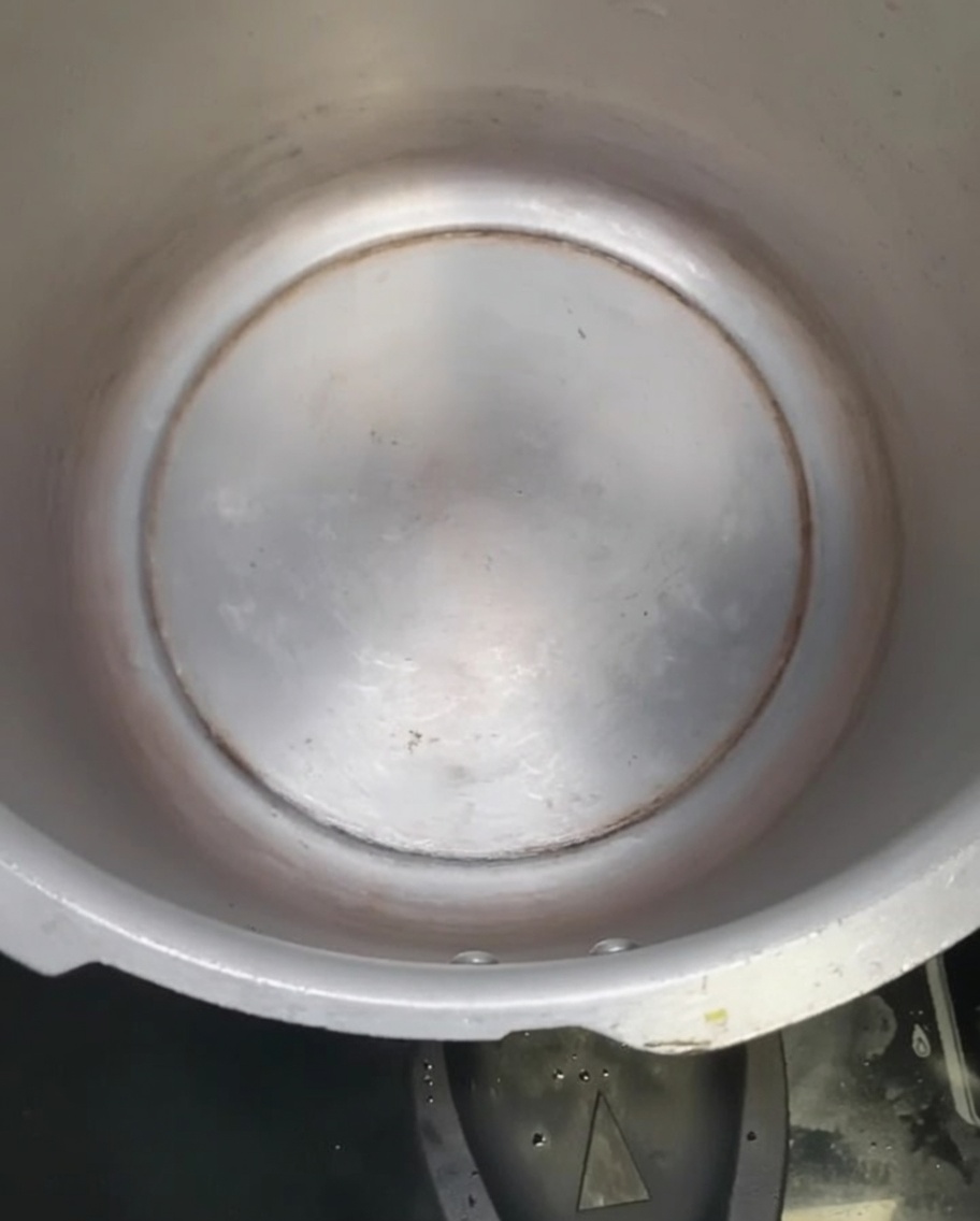 Peanut oil glistening at the bottom of an empty pressure cooker.