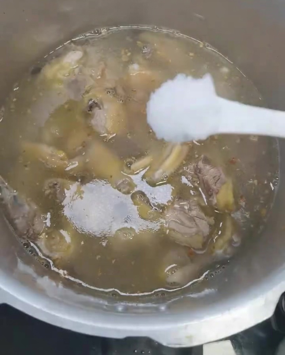 Salt being added to the chicken soup in the pressure cooker.