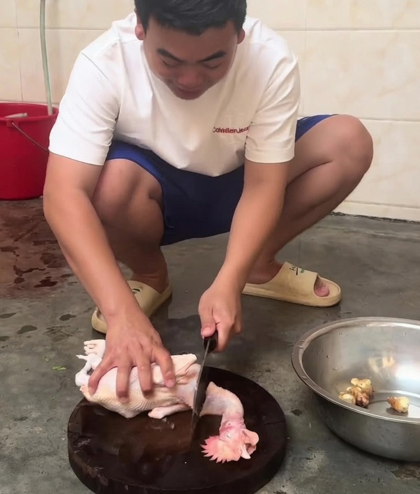 A raw whole chicken being cut into smaller pieces with a cleaver on a wooden board.