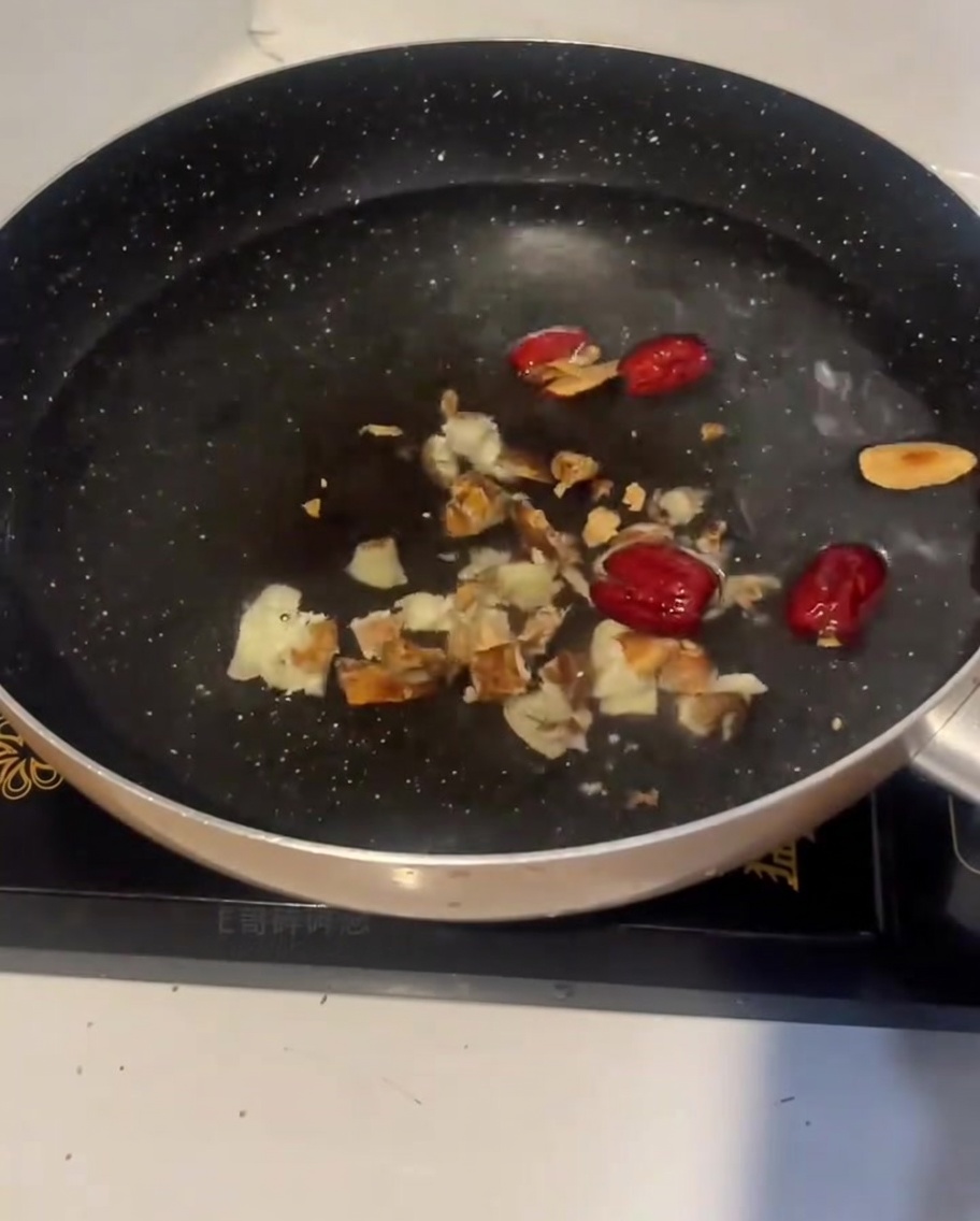 Raw chicken pieces being added to the pot of cold water with ginger and red dates.