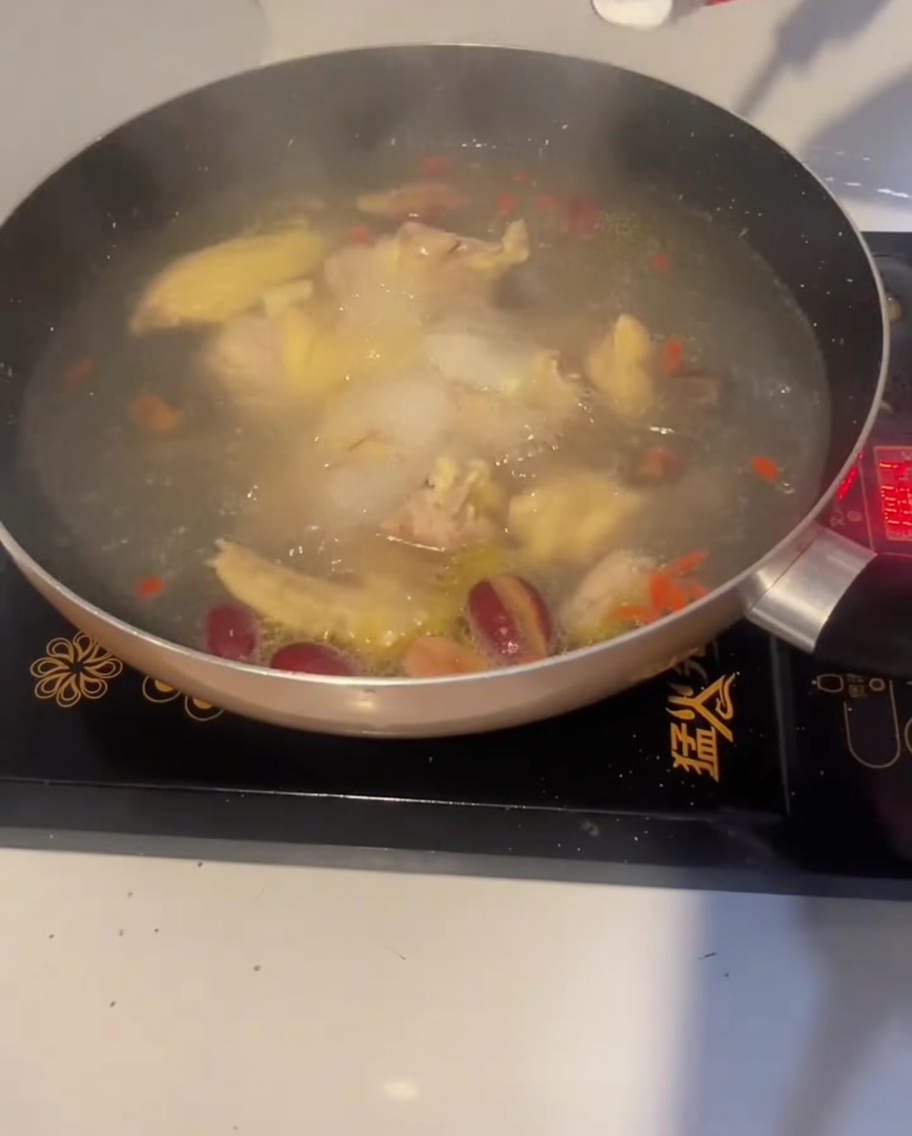 A spoonful of salt being added to the boiling chicken soup to season it.