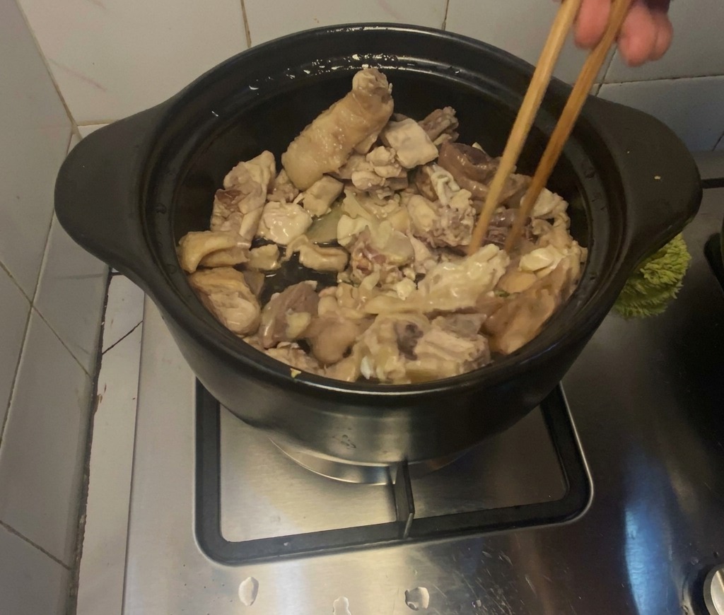 Chicken pieces being actively stir-fried with wooden chopsticks inside a black clay pot on a stovetop.