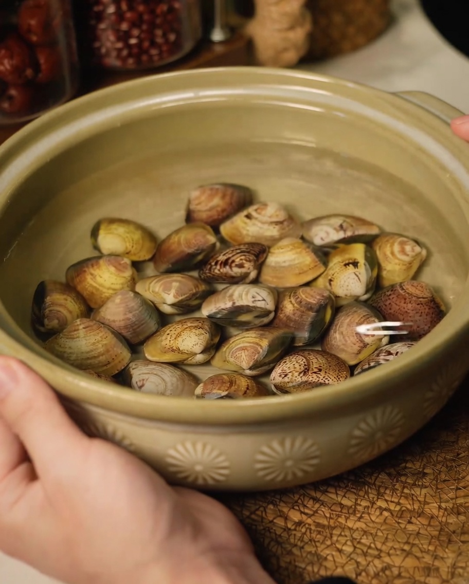 Fresh clams soaking in a ceramic bowl of water to remove sand.