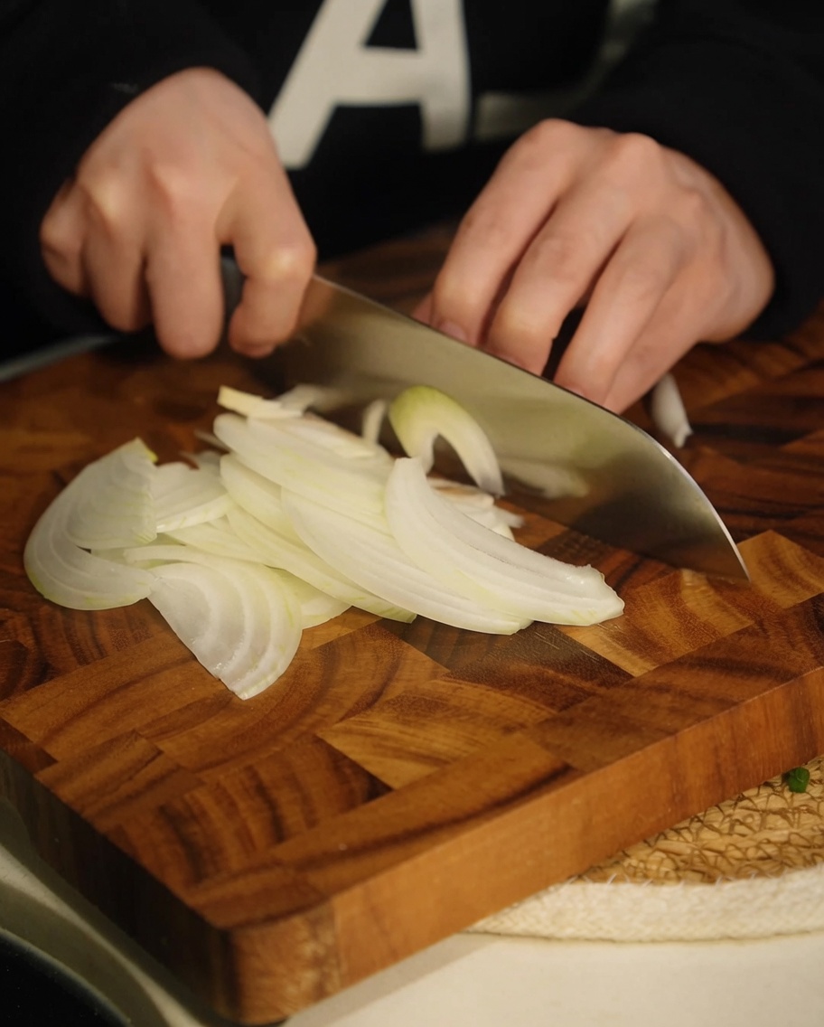 Thinly sliced white onion strips on a wooden cutting board.