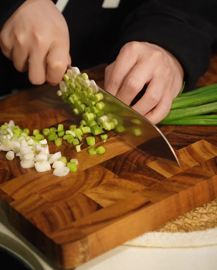 Freshly chopped green scallions on a wooden cutting board.